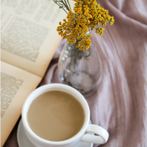 coffee cup sits next to an open book with yellow flowers